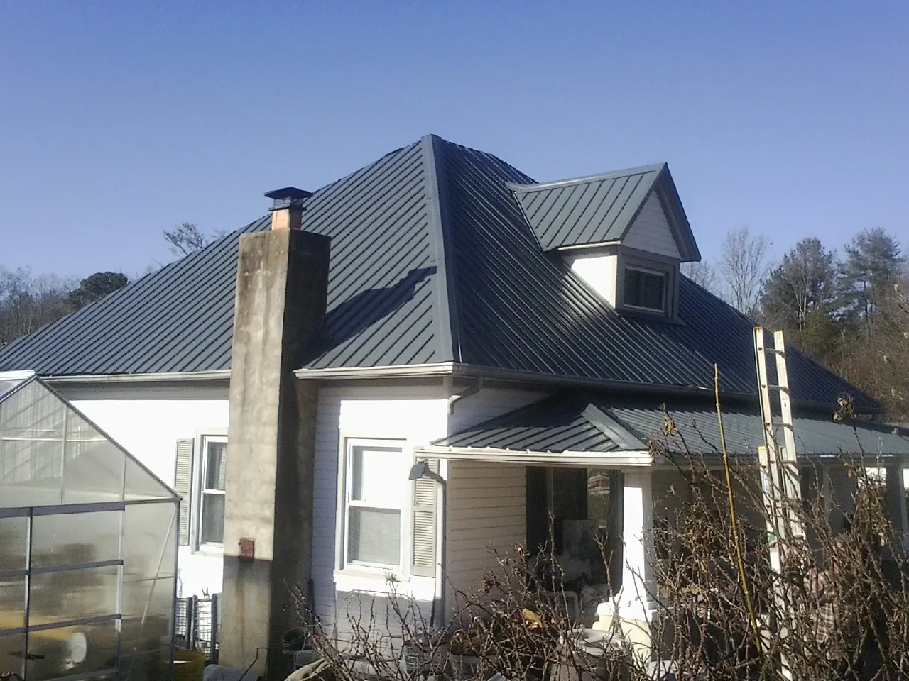 Dark blue standing seam metal roof on a white farmhouse with dormer — Slate & Tile Roof Repair by Roofing Brothers in Bonaparte