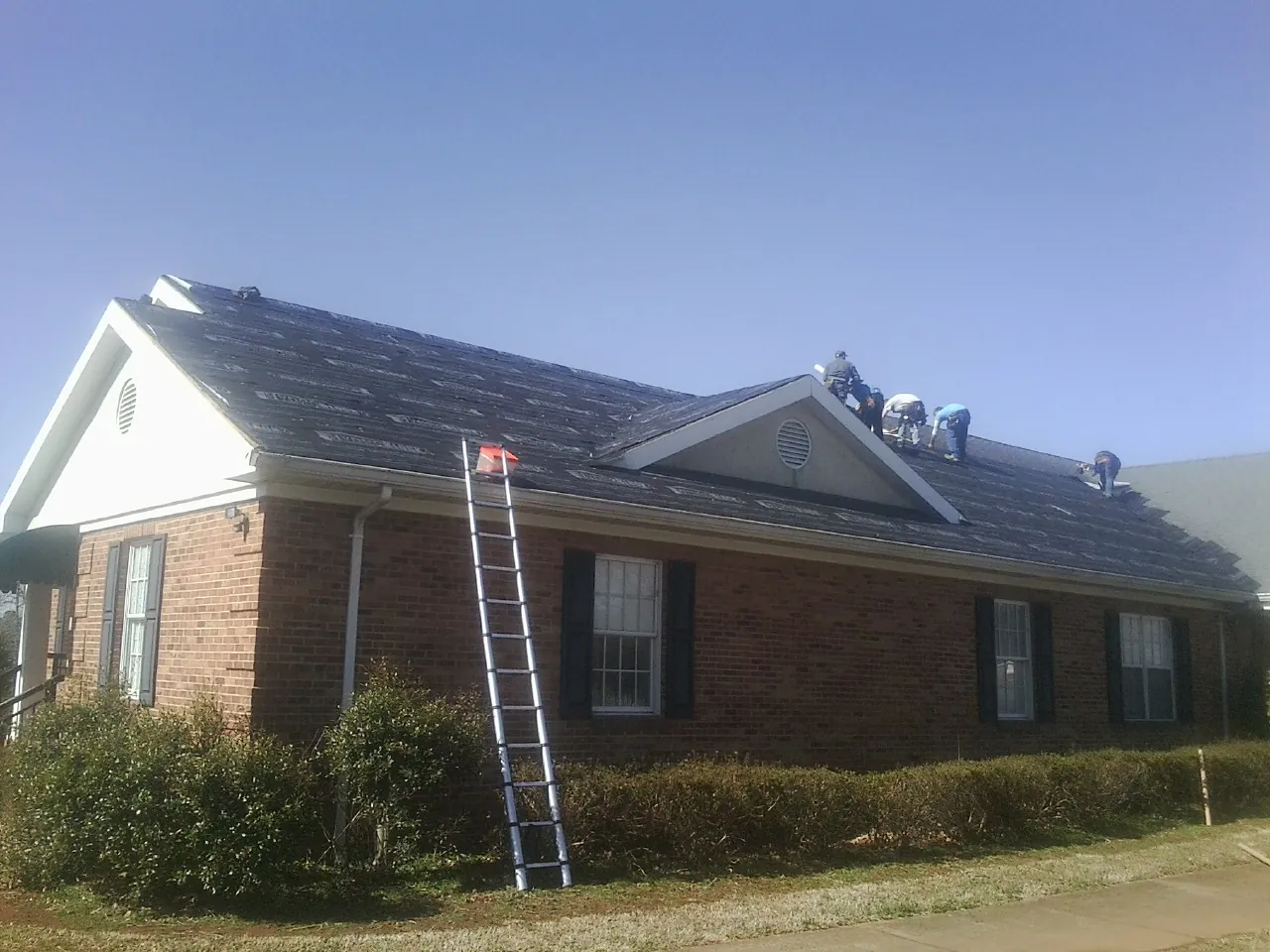 Crew tearing shingles off a brick ranch roof with a ladder set — Metal Roof Repair work by our crew in Bonaparte