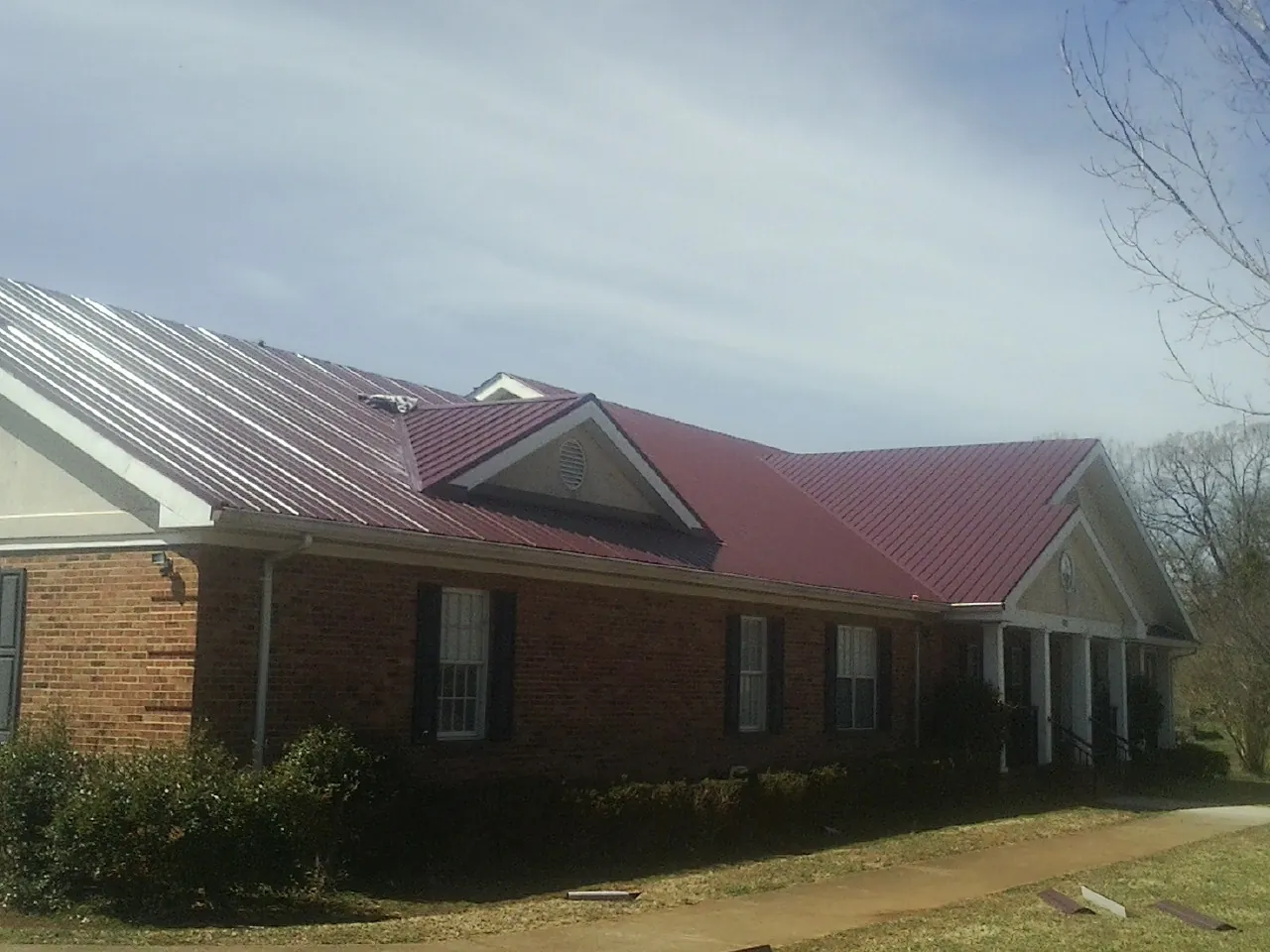 Red metal roof with gabled entries on a long brick building, from a Hail Damage Roof Repair job in Bonaparte