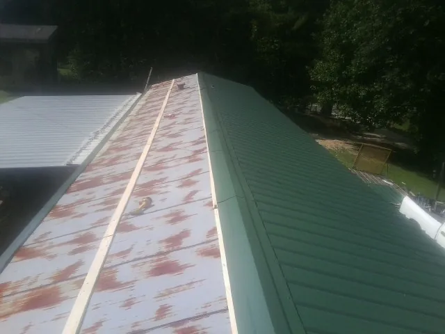 Old rusted panels beside newly installed green metal roofing — Wind Damage Roof Repair by Roofing Brothers in Bonaparte