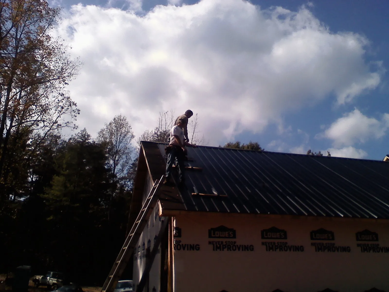 Roofer fastening dark metal panels high against a cloudy sky, from a Roof Inspection job in Bonaparte