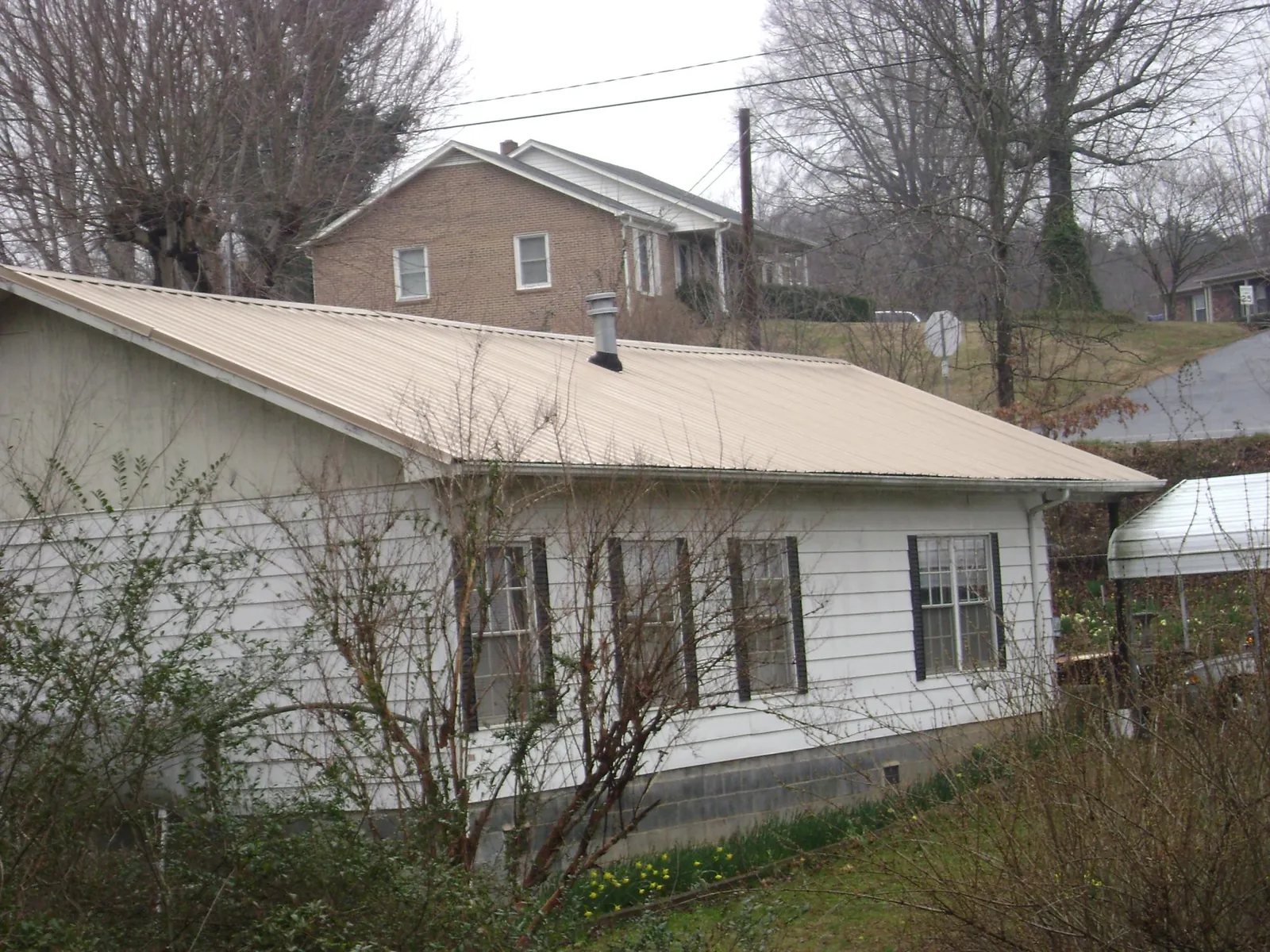 Tan metal roof on a white sided house set into a hillside — Commercial Roofing by Roofing Brothers in Bonaparte