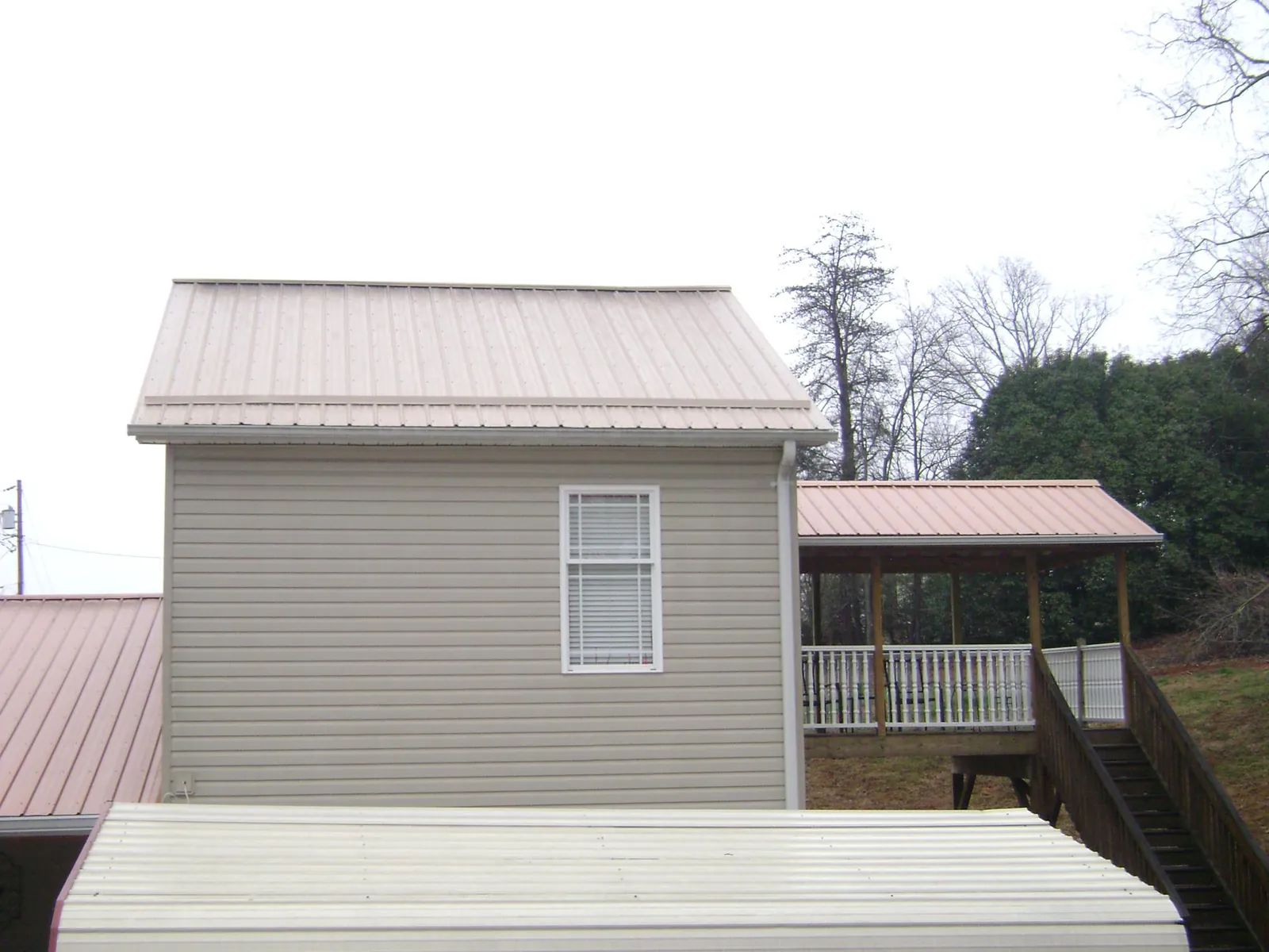 Tan metal roofs on a two story addition and attached porch, from a Roof Replacement job in Bonaparte